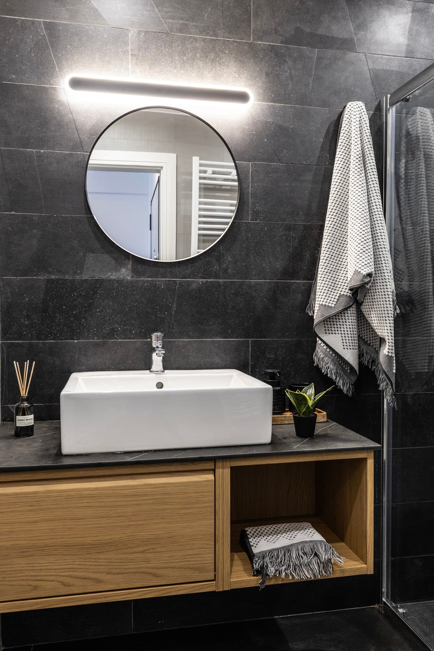 Modern bathroom with dark stone tiles and wooden storage cabinet